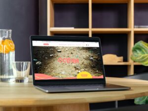 Ein Laptop auf einem Tisch mit einem Website-Mockup, links daneben eine Wasserkaraffe mit Orangenscheiben