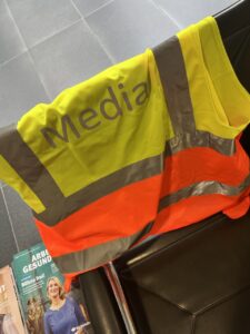 Eine Sicherheitsweste in Neon Gelb und orange mit der Aufschrift "Media" hängt über einem Stuhl